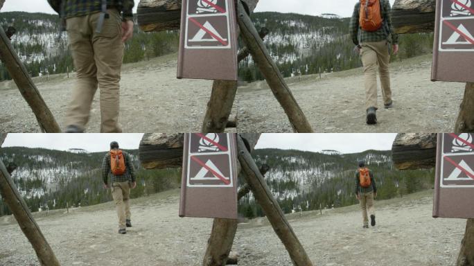 一名年轻的高加索男子背着背包，走过“禁止篝火”和“禁止露营”的路标，准备在冬季阴云密布的科罗拉多州落