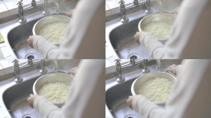 特写镜头：一位面目全非的女子在家中用滤水器从煮熟的意大利面中倒水
