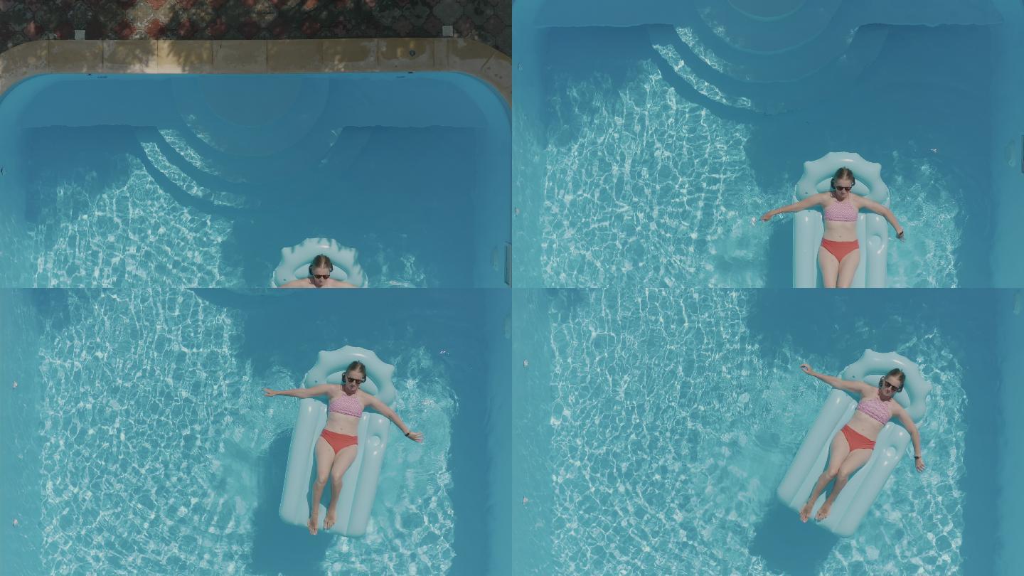 一个戴着墨镜的女人躺在游泳池里的蓝色充气床垫上。