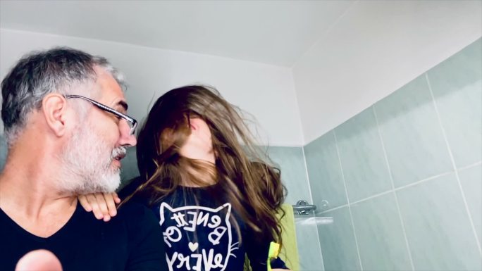 快乐的长发小女孩和父亲在浴室里摇着头