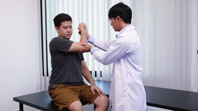 亚洲理疗师检查接受骨科康复治疗的患者的肘关节。