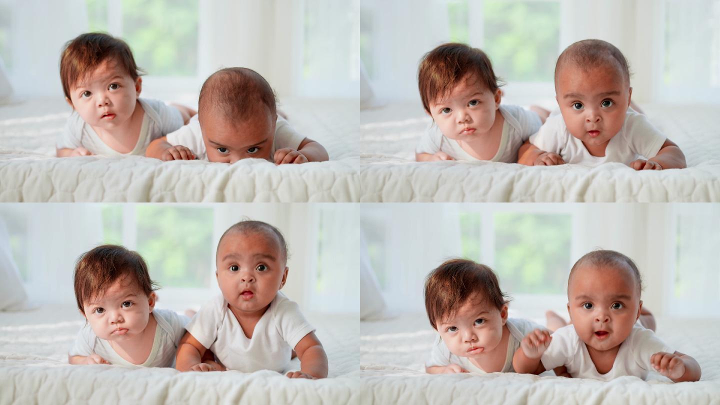 一个无辜的两个穿着白色婴儿服的黑白相间的新生儿躺在床上，试图爬行并看着摄像机。