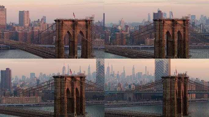 早上布鲁克林大桥上的交通，塔顶挂着美国国旗，背景是曼哈顿天际线的远景，空气透视图使其变得模糊。无人机