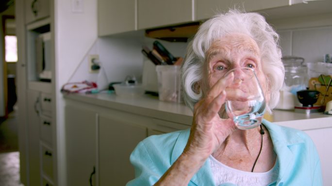 一位上了年纪的妇女在喝完橘子粉混合饮料后，整理并放下玻璃杯，以补充日常维生素或药物