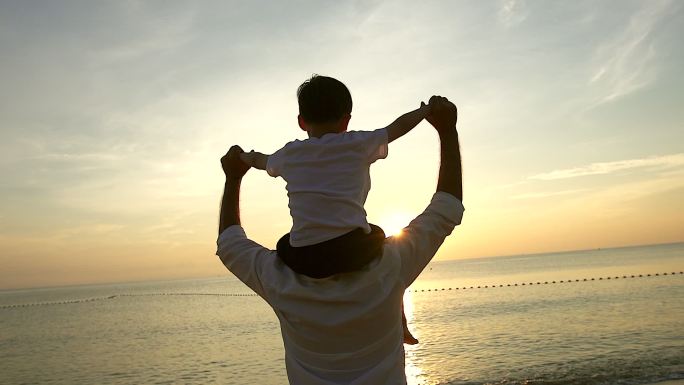 日出时分，父子俩站在海滩上，一起度过了美好的家庭时光。用慢镜头拍摄。