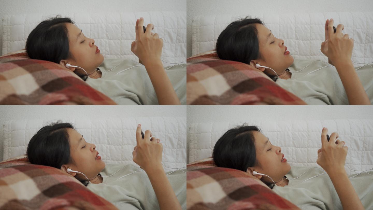 亚洲女性躺着戴耳机在智能手机上玩游戏