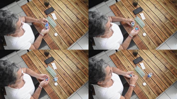 老年女性在每日药丸管理器中放置药物的俯视图