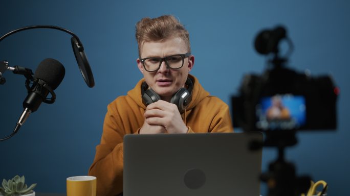一位年轻可爱的金发博主用专业设备在工作室为他的播客录制视频