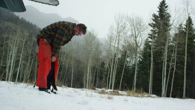 在大雪纷飞的冬日，一位30多岁留着胡子的白种人在森林里穿上电锯安全裤