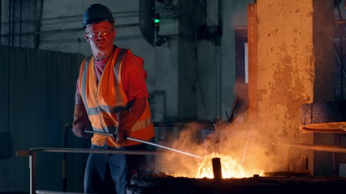 男工人在铸造厂清除熔融金属中的熔渣