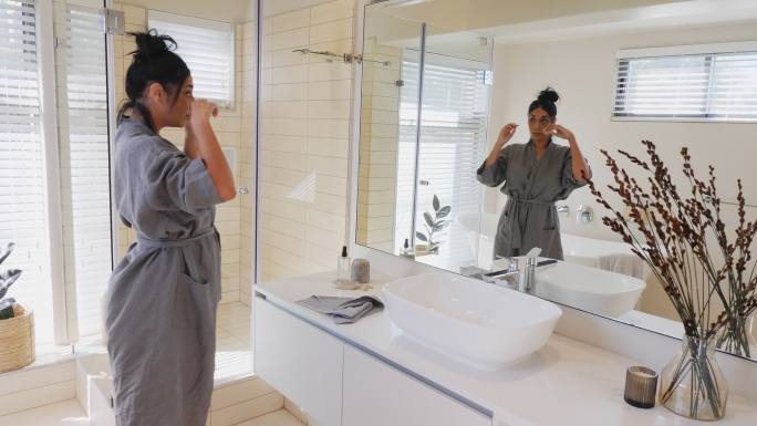 穿着浴袍的美女在豪华浴室镜子里整理头发