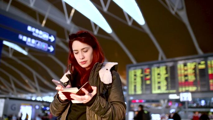 航班取消后，一名年轻女子在机场候机楼用手机上网查找另一名乘客