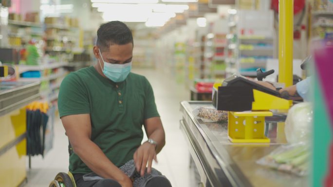 周末，亚裔印度残疾男子坐轮椅在收银台超市退房