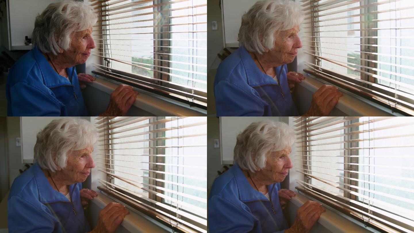 一位年长的白人妇女站在室内透过百叶窗向外看