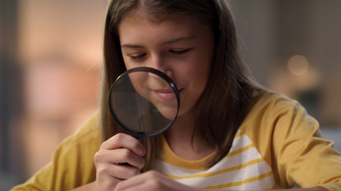 一个年轻女孩独自坐在家里，一边做科学作业，一边使用放大镜的4k视频片段