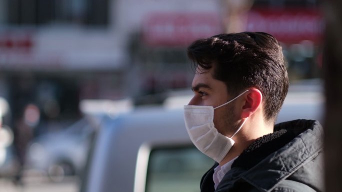 脸上戴着医用面罩的年轻人站在城市街道上