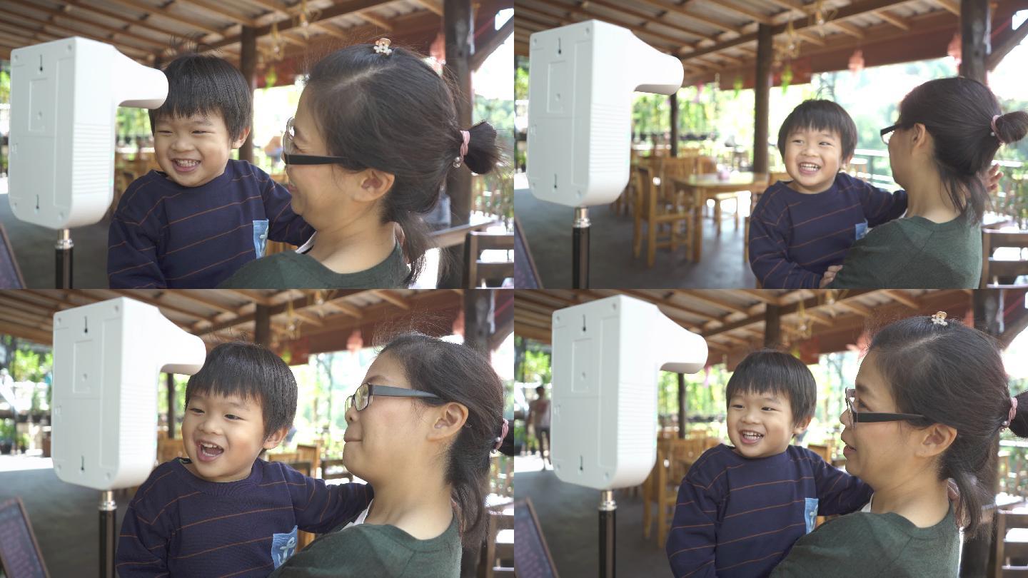 亚洲母亲抱着儿子用数字热扫描仪测量体温