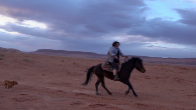 纳瓦霍族在亚利桑那州纪念碑谷的土地上骑马，背景是标志性的纪念碑