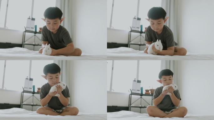 戴着精灵耳环的亚洲男孩在卧室里玩兔子。