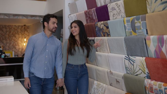 一对美丽的年轻夫妇在一家纺织店看着零售展示，边走边聊边笑