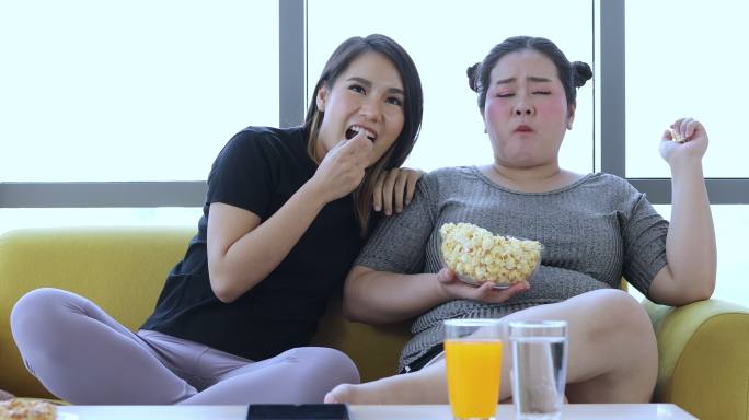 身材高大的女人和亚洲女孩喜欢在家里的沙发上吃东西