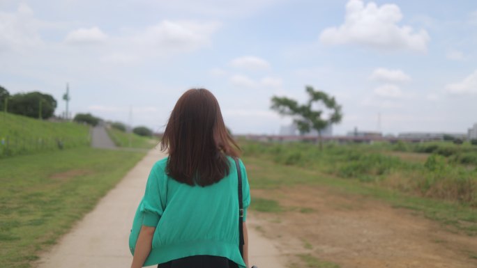 穿着绿色开衫的女子在河岸上行走的后视图