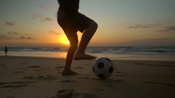 日出时在海滩上打球的男孩的剪影