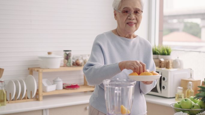 亚洲老年女性，80岁，用电动搅拌机自己准备水果冰沙，享受健康饮食、侧视、城市生活的老年人、退休后独处