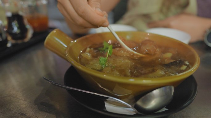 曼谷唐人街Yaorawat一家街头美食餐厅的金属桌上，用塑料勺在碗里搅拌热鱼肚汤。亚洲人手