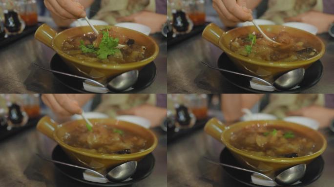 曼谷唐人街Yaorawat一家街头美食餐厅的金属桌上，用塑料勺在碗里搅拌热鱼肚汤。亚洲人手