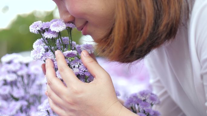 年轻女子幸福地捧着一朵紫花，闻着花园里的紫花