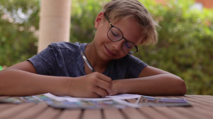 十几岁的男孩坐在后院的桌子旁写明信片