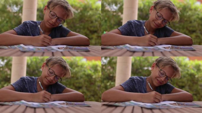 十几岁的男孩坐在后院的桌子旁写明信片