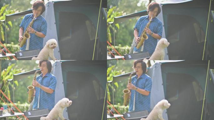 早上，亚裔中国萨克斯管演奏家和他的宠物玩具贵宾犬在露营帐篷前演奏