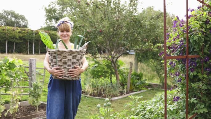 写真快乐的女人在后院花园收获新鲜蔬菜