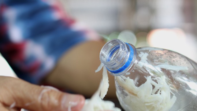 一只手拿着一片竹笋塞进塑料瓶。