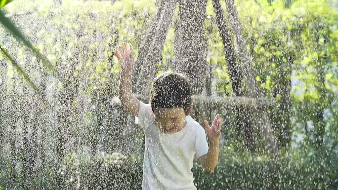 炎热的夏天，一个小男孩在后院的喷水器里玩耍。（使用慢动作vdo摄像机拍摄）