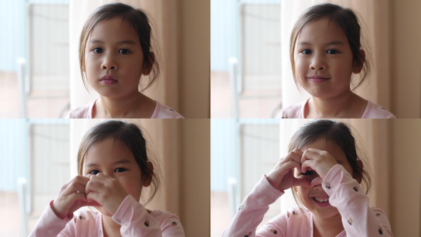 4K慢镜头，快乐的亚裔混血小女孩用手捂住眼睛做心形手势，捐赠、慈善、关怀、爱、心脏健康、社交距离概念