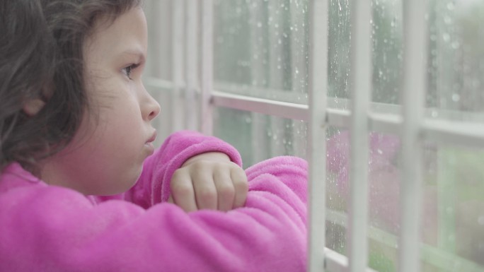一个拉丁女孩在家里看着窗外的雨