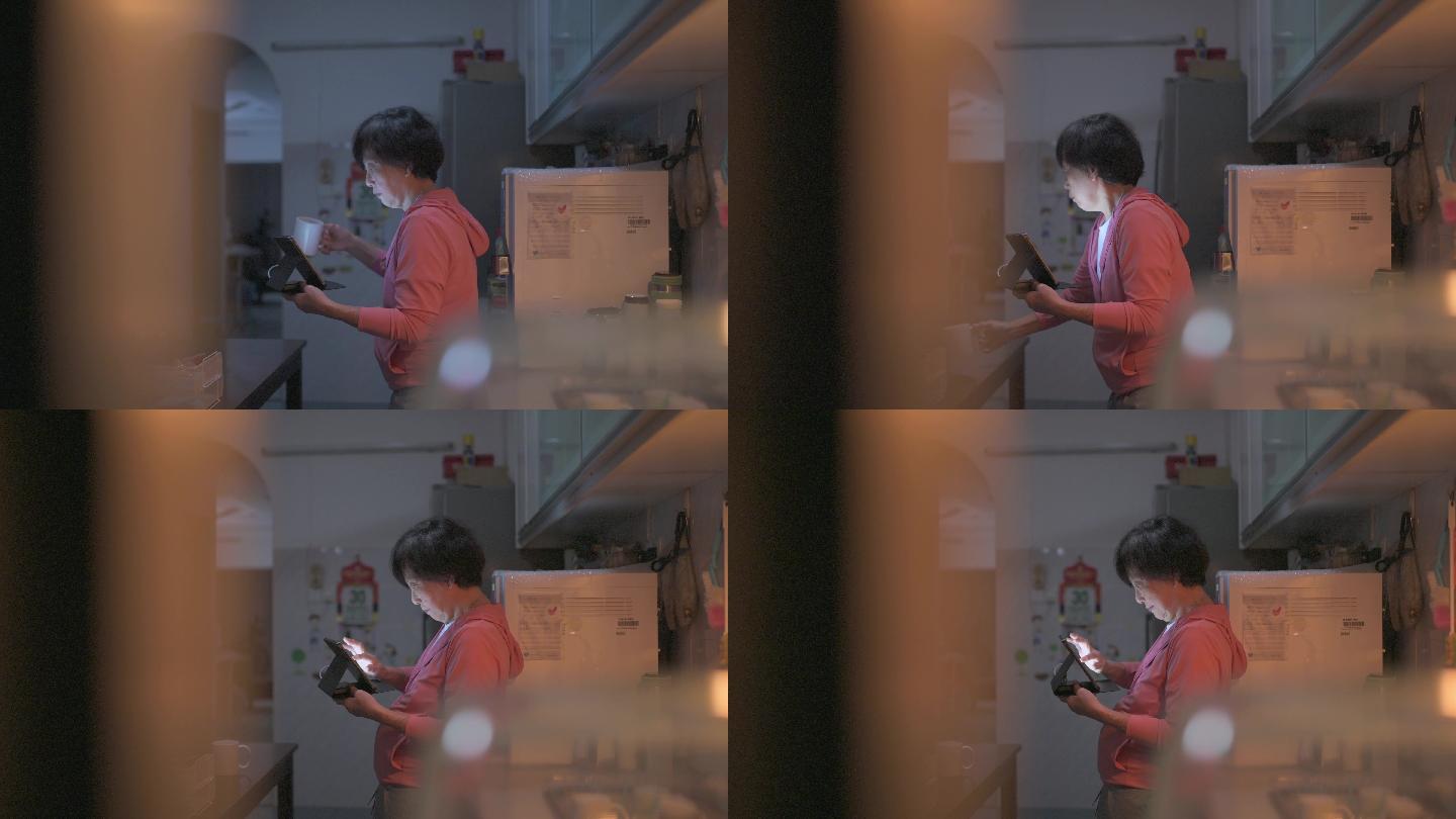 亚裔中国老年女性晚上在家庭厨房使用数码平板电脑和饮用水上网