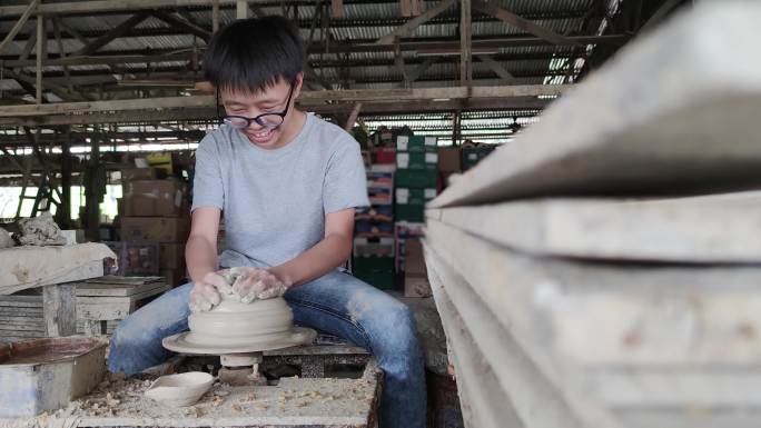 亚洲的中国少年正在陶轮上制作一个泥碗。他正在愉快地展示他的产品产量。