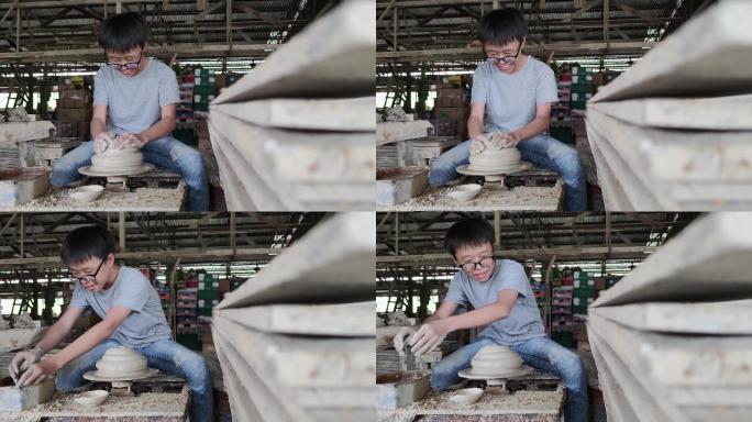 亚洲的中国少年正在陶轮上制作一个泥碗。他正在愉快地展示他的产品产量。
