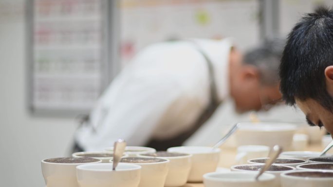 专业亚裔中国男咖啡师品级师在咖啡杯上弯腰，仔细闻每一杯咖啡