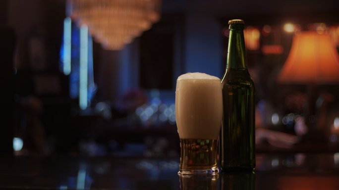 一座有酒吧的豪宅里昏暗的起居室，里面有一瓶啤酒和一个玻璃杯