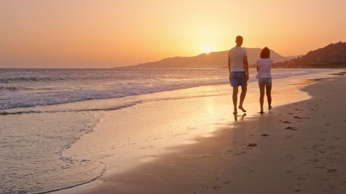 夕阳西下，父女俩在沙滩上散步聊天