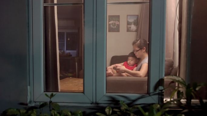 晚上，母亲和男婴在家客厅的沙发上一起看智能手机
