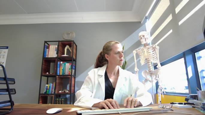 女性医院总经理正在制作桌面式内容，背后是人体骨骼