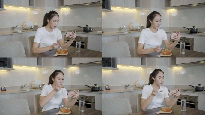 一名穿着睡衣、喉咙痛的亚洲女子正在家中厨房的桌子上吃鸡汤以缓解喉咙痛，并与朋友视频通话