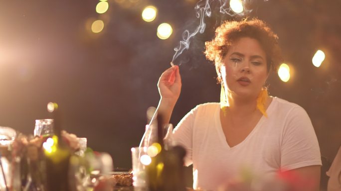 一位年轻女子在后院与朋友一起享受晚餐时吸烟