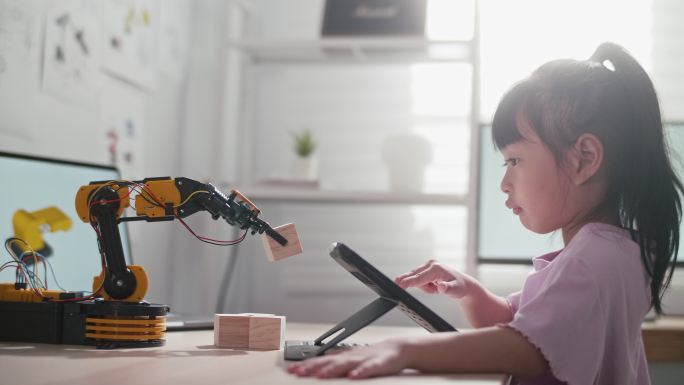 一个女孩正在学校玩机器人手臂。他正在用手控制它。